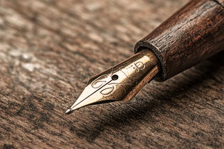 An antique metal pen tip on a wood desk.